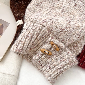 Close-up of beige chunky knit fabric with mixed threads and a decorative wooden button