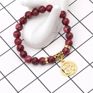 Détail d'un bracelet en perles rouges tachetées avec breloque Om dorée sur support