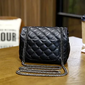 Borsa a tracolla trapuntata nera con borchie metalliche e catena su tavolo di legno