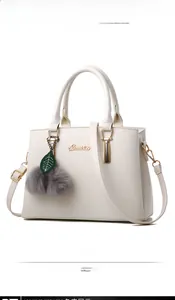 Detail of cream trapezoid handbag with gold logo and soft grey faux fur pompom charm