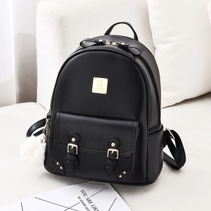 Sac à dos femme en cuir souple noir avec noeud et pompon posé sur un canapé blanc