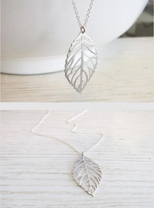 Close-up and flat lay view of a silver leaf pendant necklace on a wooden surface