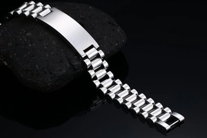 Polished silver stainless steel watch-style bracelet resting on a textured black stone surface