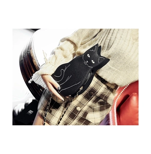 Detail of a black cat-shaped crossbody bag with gold chain strap worn by a model