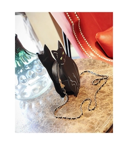Close-up of a black cat-shaped chain crossbody bag placed on a marble table with a red chair