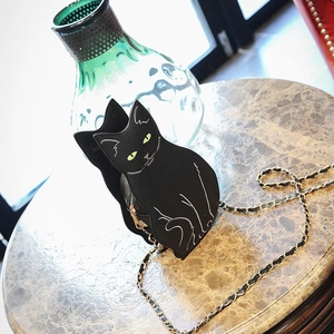 Detail of creative black cat crossbody bag with green eyes and golden chain strap