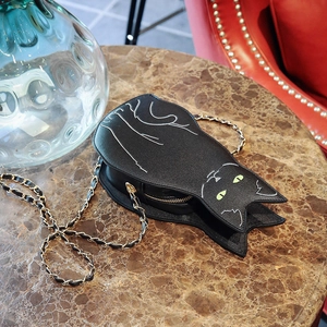 Detailed view of cat-shaped handbag with golden chain strap on marble surface
