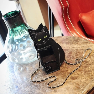 Detail of black cat shaped leather crossbody bag with chain next to a smartphone