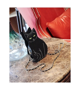 Chic black cat chain bag with green embroidery on marble table with red chair background