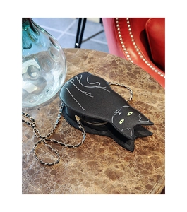Detail shot of a black cat-shaped crossbody bag with gold chain on a marble table