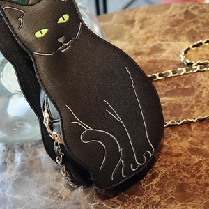 Detailed view of a black cat-shaped crossbody bag with white stitching and green eyes