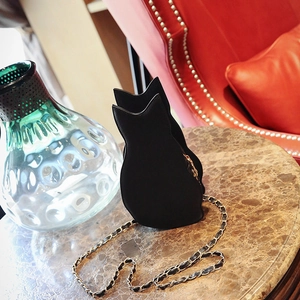 Detail of a black cat-shaped crossbody bag with gold chain strap on marble surface