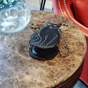 Detail view of a black cat-shaped crossbody bag with a gold chain on a marble table