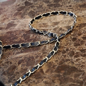 Detailed macro view of gold metal chain woven with black leather on marble background