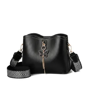 Détail d'un sac en cuir PU noir avec pendentif papillon doré et bandoulière rayée