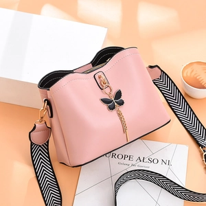 Sac seau en cuir rose avec pendentif papillon et bandoulière géométrique sur fond orange