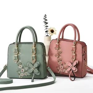 Close-up of floral embroidery and bow pendant on vintage-style leather tote bag