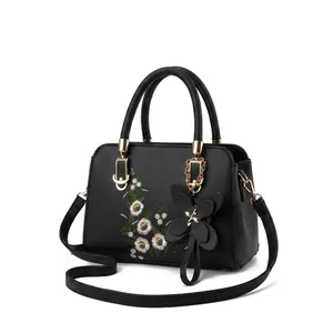 Detailed embroidery of small white and purple flowers on a black leather handbag surface