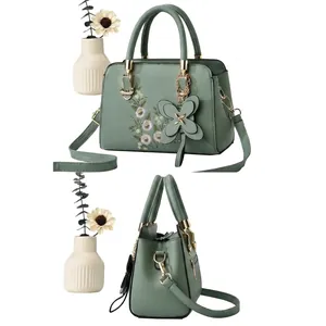 Detail of sage green handbag featuring delicate floral embroidery and leather butterfly charm