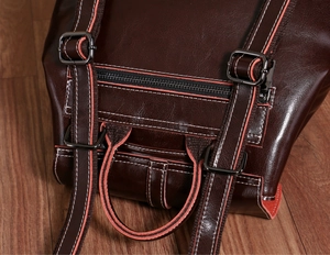 Detail of dark brown leather backpack showing sturdy handle, metal buckles and zip pocket