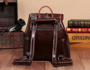 Detail view of the back of a brown oil wax leather backpack showing straps and zipper pocket