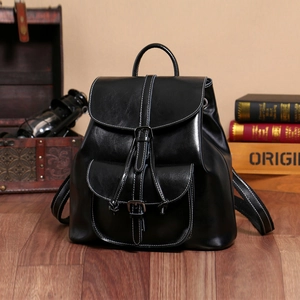 Detailed view of black wax cowhide leather backpack with front pocket on wooden floor
