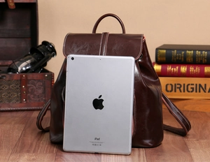 Deep brown oil wax leather backpack shown next to an iPad for size reference