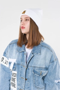 Detail of light blue denim jacket with patches and white knitted beanie on model