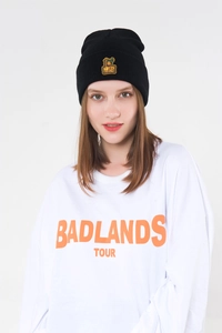 Close-up of black knitted beanie with monkey patch and white long-sleeved shirt