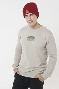 Detail of red knitted beanie with cartoon monkey patch worn with a grey crewneck sweatshirt