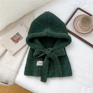 Detail of green chunky knit balaclava hat with adjustable ties and a woven label