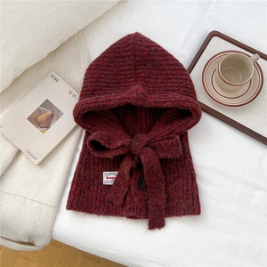Detail view of burgundy knitted balaclava with button and ribbon on soft fabric