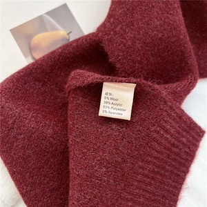 Close-up of wine red knit scarf showing material texture and detailed wash label