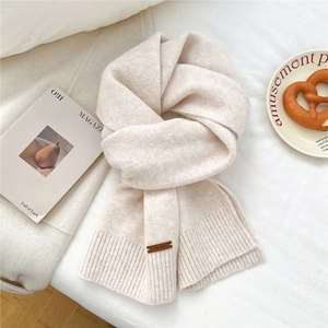 Detail of soft cream knitted scarf featuring thick texture and brown leather label