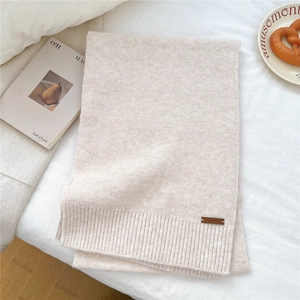 Close-up of beige knit scarf texture with a brown leather brand tag on soft bedding