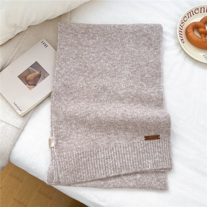 Detail of oat-colored knitted scarf with leather logo and ribbed texture on fabric