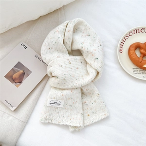 Detailstruktur des cremefarbenen Strickschals mit bunten Konfetti-Punkten und Stoffetikett