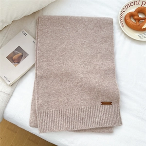 Detail of soft beige knitted scarf featuring ribbed edges and a premium leather brand tag
