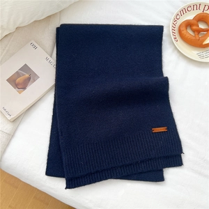 Close-up of dark blue knit scarf texture with a leather label on soft white fabric