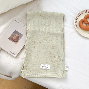 Makro-Detail von cremefarbenem Strickschal mit Sprenkelmuster und dekorativem Markenaufnäher
