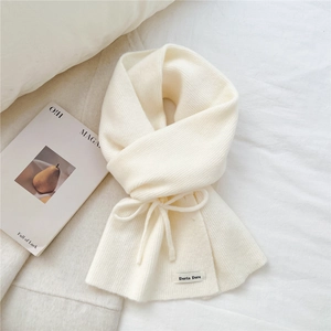 Macro detail of creamy knitted scarf texture with bow tie and minimalist brand label