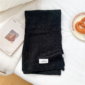 Flachbildaufnahme des schwarz gesprenkelten Strickschals mit Markenlabel und gemütlichem Stil