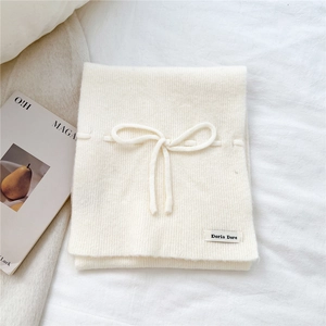 Detail of soft cream knitted scarf featuring ribbon bow and minimalist logo label