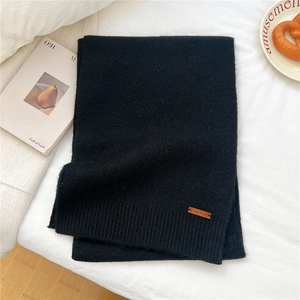 Detailed close-up of black knit scarf with leather patch on cozy white fabric surface