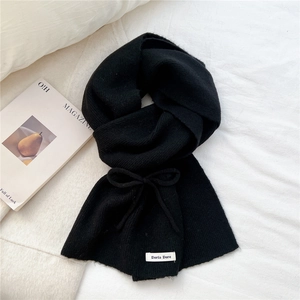 Close-up of black knitted scarf with vertical stripes and bow detail on fabric