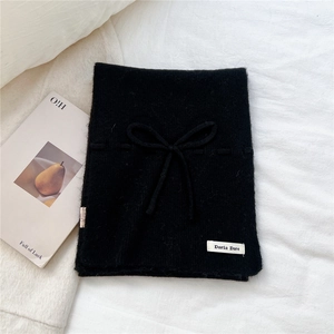 Detail of a soft black knitted bow scarf with white brand label on white texture background