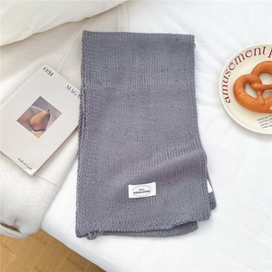 Detail eines grauen Grobstrickschals mit bunten Tupfen und gewebtem Markenlabel