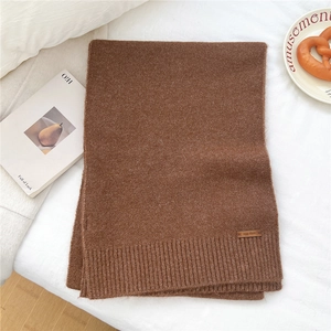 Macro detail of caramel brown knit scarf texture showing the premium leather brand label