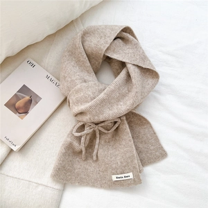 Detail view of oatmeal knit scarf with a bow design and a woven brand label