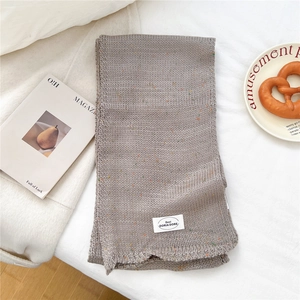 Detail eines hellgrauen Strickschals mit bunten Tupfen und weißem Markenetikett